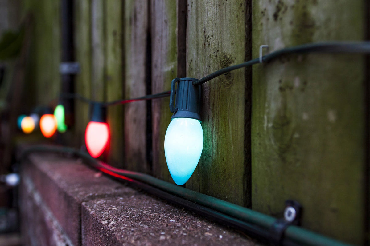 Colorful, smooth-finish LED Christmas lights on a wire against a wooden fence.